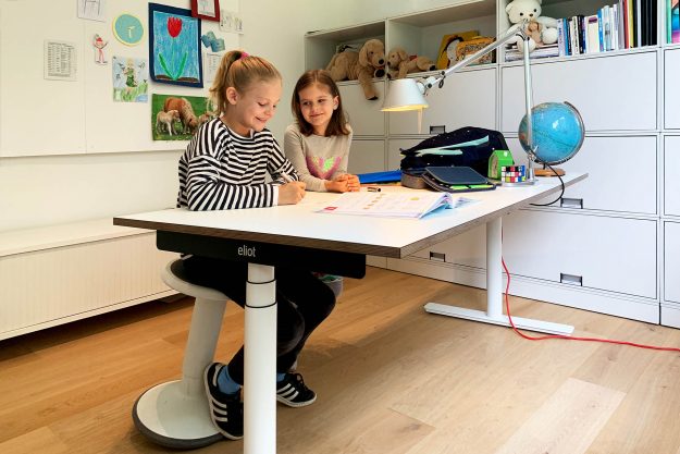 Kinder in Kinderzimmer mit höhenverstellbarem Schreibtisch.