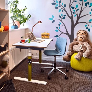 Ein Kinderzimmer mit Laptop auf einem weißen höhenverstellbaren Schreibtisch mit rotem Kabel und gelben Füßen.