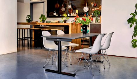 Offener Büroraum neben Küche mit schwarzem Schreibtisch und grauen Stühlen.