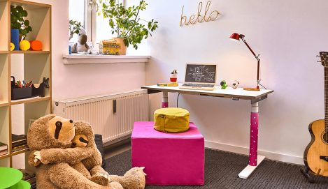 Ein Kinderzimmer mit Laptop auf einem weißen höhenverstellbaren Schreibtisch mit rotem Kabel und pinken Füßen.