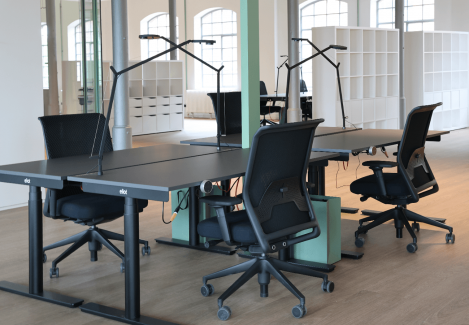 Ein Konferenzraum mit höhenverstellbaren Schreibtischen und Stühlen und Lampen.