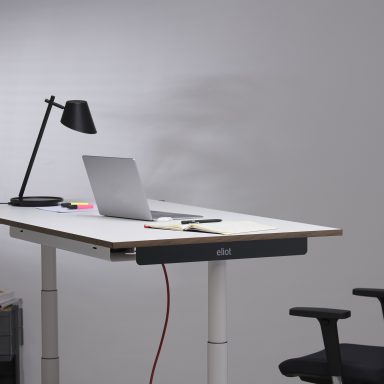 Laptop auf einem weißen höhenverstellbaren Schreibtisch mit rotem Kabel.