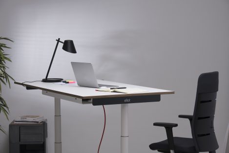 Laptop auf einem weißen höhenverstellbaren Schreibtisch mit rotem Kabel.